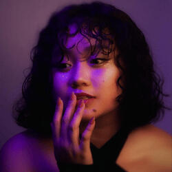 Portrait of MIZI, a female DKLT Designs team member, with purple lighting, posing with her hand near her face.
